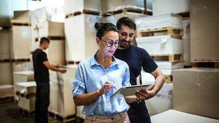 Two workers in warehouse looking at iPad