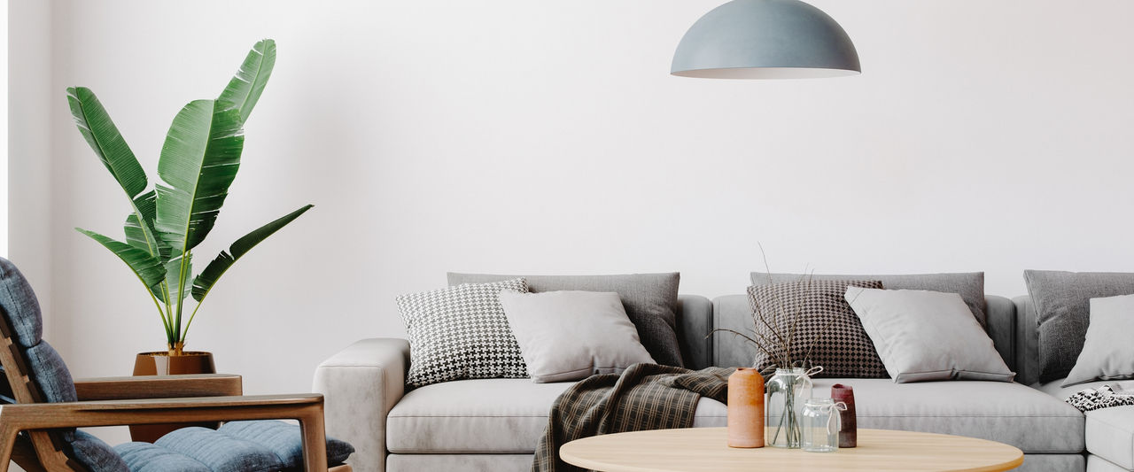 Modern living room setup with classic parquet floor. Furnished with light gray sofa, blue arm chair with wooden frame, modern blue ceiling lamp, wooden coffee table and gray carpet.